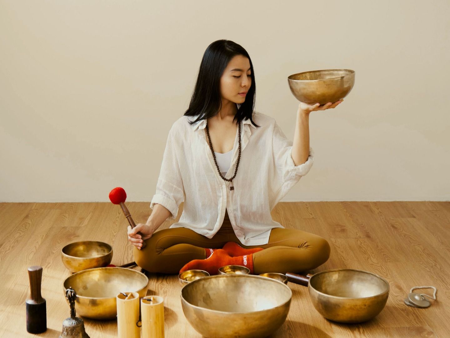Instructor seated among singing bowls, one bowl raised, during a sound bath